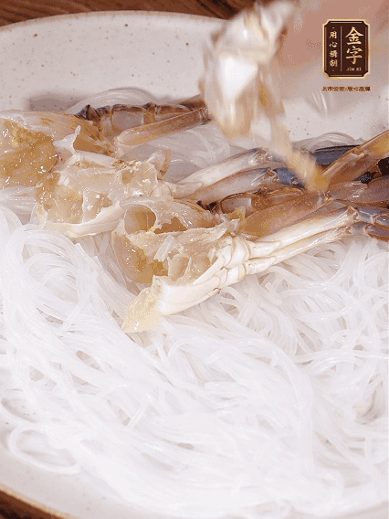 盤底墊上粉絲，擺上梭子蟹、火腿片，撒姜粒，淋上蒸魚豉油、花雕酒調(diào)味腌制15分鐘